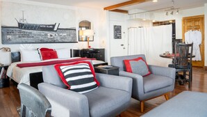 A hotel room with a bed, two grey armchairs, a small table, a desk, and a wardrobe. - Outer Island Apartment @ The Copper Crown (Bayfield)