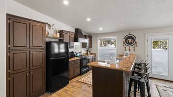 A kitchen with dark wooden cabinets, a black refrigerator, a granite countertop, and a large window.