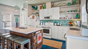 A kitchen with white cabinets, a central island with stools, a microwave, an oven, and a sink. - `Escape to Endless Summer: Morning coffee, and BBQs, with access to two community pools for endless family fun!` (Port Aransas)