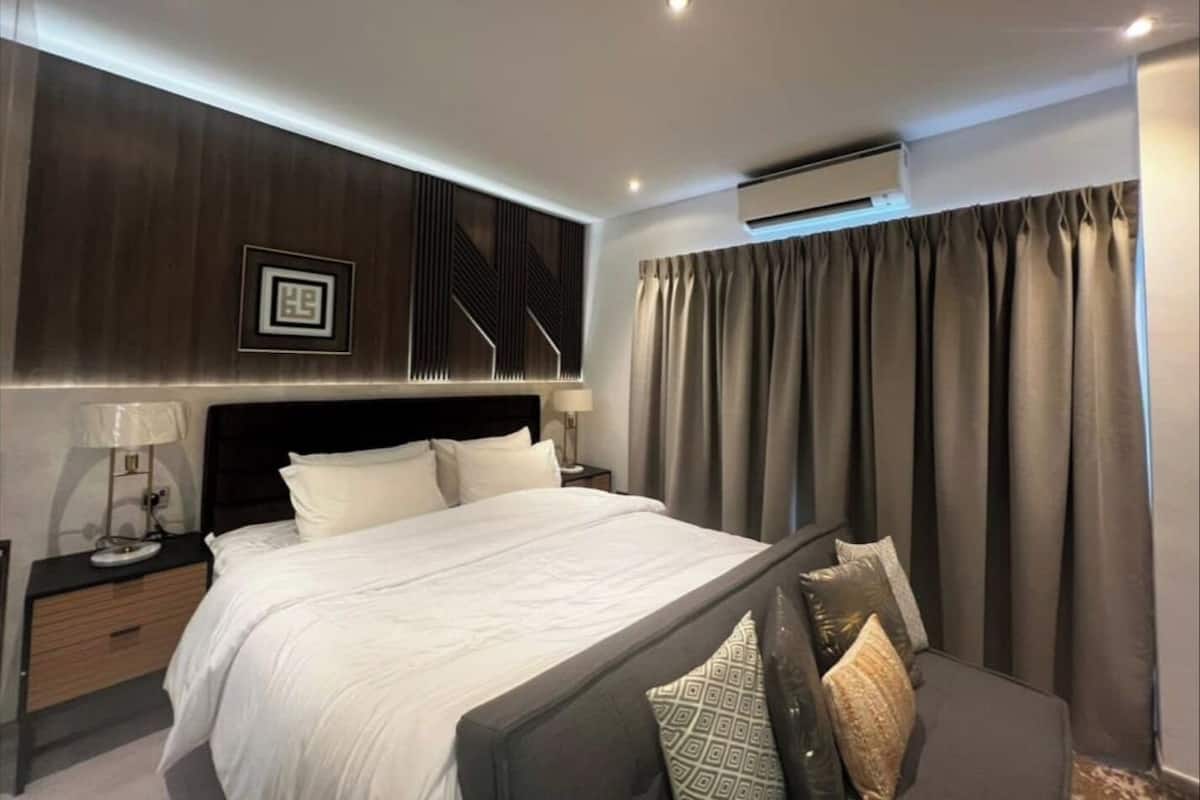Ein modernes Schlafzimmer mit einem großen Bett, einem Nachttisch, einer Lampe und einer wandmontierten Klimaanlage.
