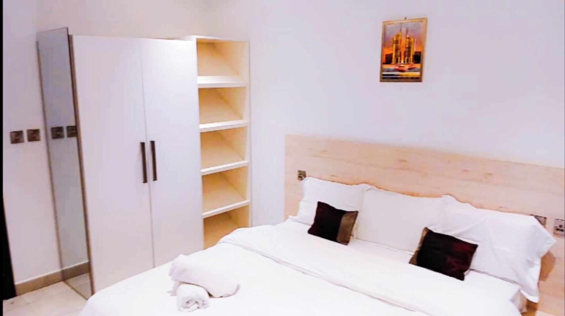 A hotel room with a bed, a wardrobe, and a painting on the wall.
