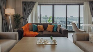 Un salon moderne avec un canapé, des fauteuils, une table basse et une vue sur la ville grâce à de grandes fenêtres.