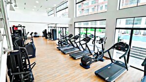 Une salle de sport spacieuse, équipée de plusieurs tapis de course, de machines de musculation et d’une grande fenêtre offrant une vue sur l’extérieur.