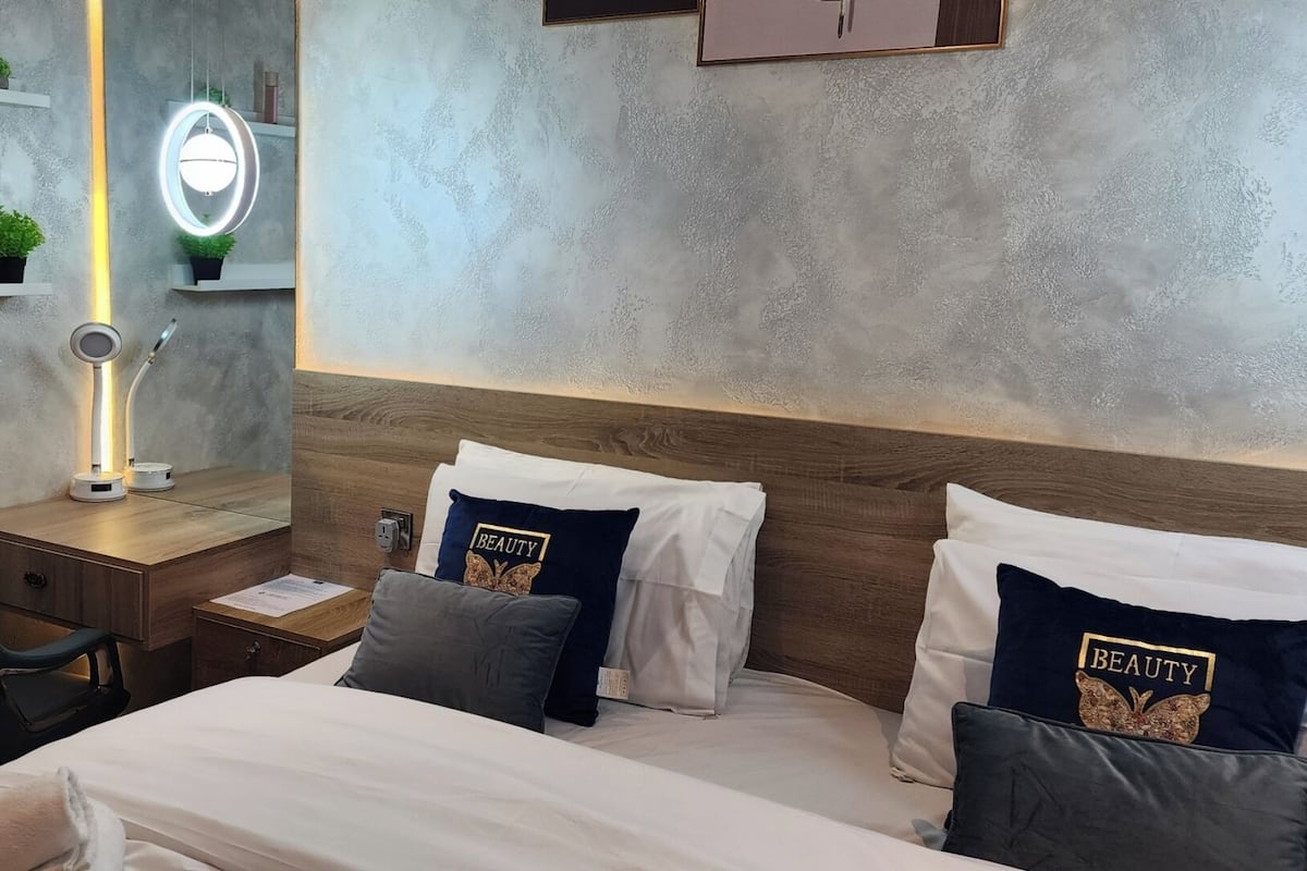 Ein Hotelzimmer mit Bett, Nachttisch, Stuhl und einem an der Wand befestigten Spiegel mit Beleuchtung.