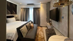 Une chambre d’hôtel moderne dotée d’un grand lit, d’un canapé, d’un téléviseur fixé au mur et d’une grande fenêtre avec des rideaux.