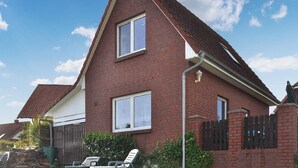 Ein zweigeschossiges Backsteinhhaus mit geneigtem Dach, einem sichtbaren Schornstein und einem kleinen Vorgarten mit Holzzaun und Stuhl.