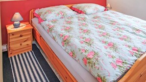 Ein Bett mit Blumenmuster auf der Bettwäsche, ein Nachttisch mit Lampe und ein Streifen Teppich.