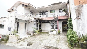 Um edifício de dois andares com varanda, escadaria e um pequeno jardim com plantas em vasos.