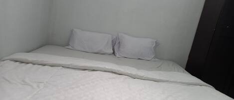 A small, single-bed room with white bedding and a plain wall.