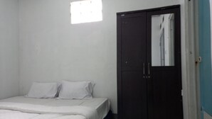 Quarto com cama, roupa de cama branca, um guarda-roupa escuro e uma janela pequena.
