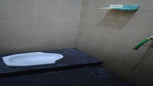 Um banheiro pequeno com azulejos, um vaso sanitário sanitário, um dispensador de álcool em gel verde e uma prateleira branca.