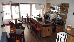 Zona de bar amb una barra llarga, diverses opcions de seients i una varietat de botelles i gots a les prestatgeries.
