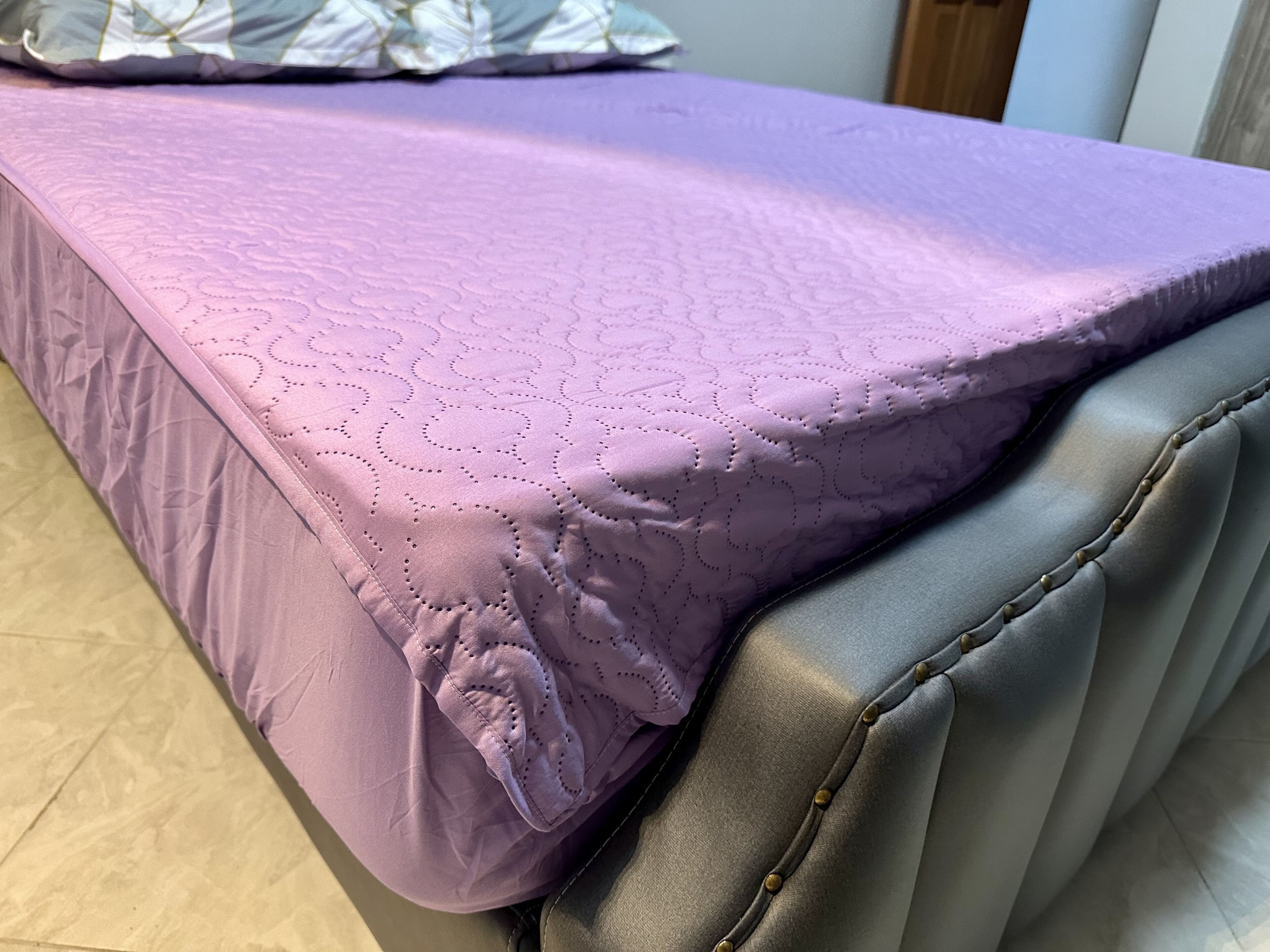 Een bed met een paarse quilt en een grijs hoofdeinde.