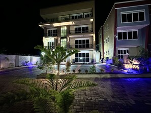 Un hotel de varios pisos con una entrada bien iluminada y un patio ajardinado.