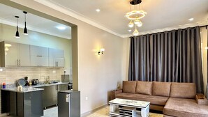 A modern living room with a sectional sofa, a coffee table, and a kitchen area with cabinets and a refrigerator.
