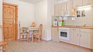 A compact kitchen with wooden cabinets, a dining table with chairs, a coffee maker, and a small oven. - Ferienwohnung Mönchgut (Mönchgut OT Alt Reddev)
