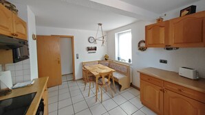 Une cuisine avec des meubles de rangement en bois, une table à manger avec des chaises, un four encastré et une fenêtre donnant sur un beau paysage.