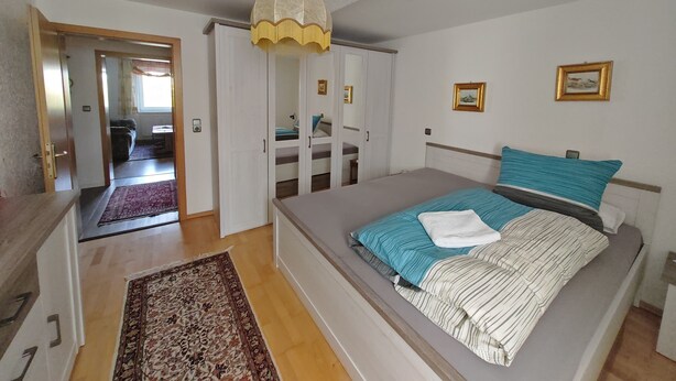 Une chambre à coucher comprenant un lit, une armoire, un miroir et un luminaire suspendu.