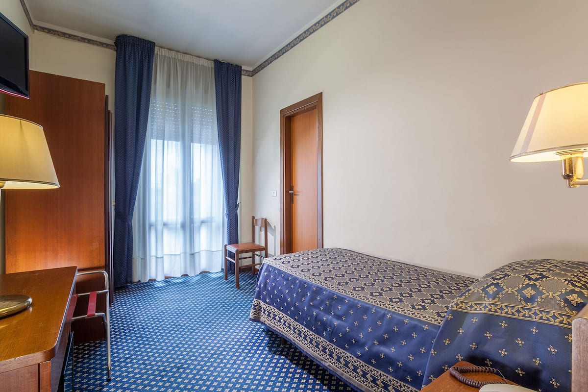 Hotellihuone, jossa on sänky, työpöytä, tuoli, vaatekaappi ja ikkuna, jossa on verhot.