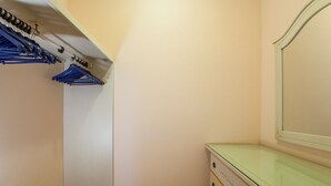 Una habitación pequeña y estrecha, con suelo de madera, una puerta blanca, un aparador de vidrio con cajones y un perchero con prendas colgadas.