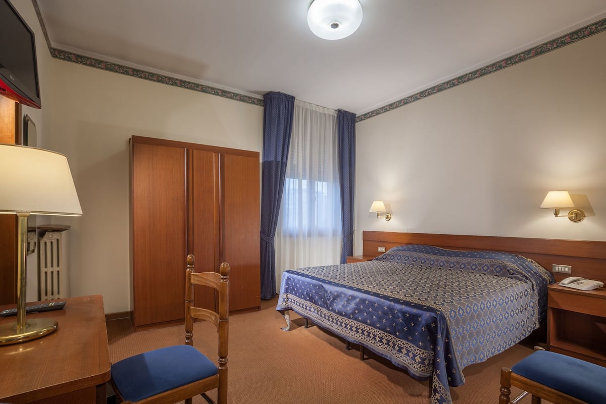 Hotellihuone, jossa on sänky, kaksi yöpöytää, työpöytä lampun kanssa, tuoli, vaatekaappi ja televisio.