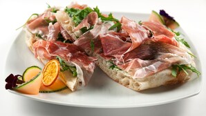 Un plato con dos rebanadas de pan cubiertas de jamón serrano y rúcula.