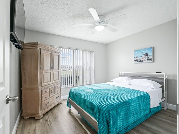 A bedroom with a bed, a wardrobe, a ceiling fan, a window with blinds, and a painting on the wall. - Escape to Luxury: Designer Pool Home in Valle Verde! (The Villages)