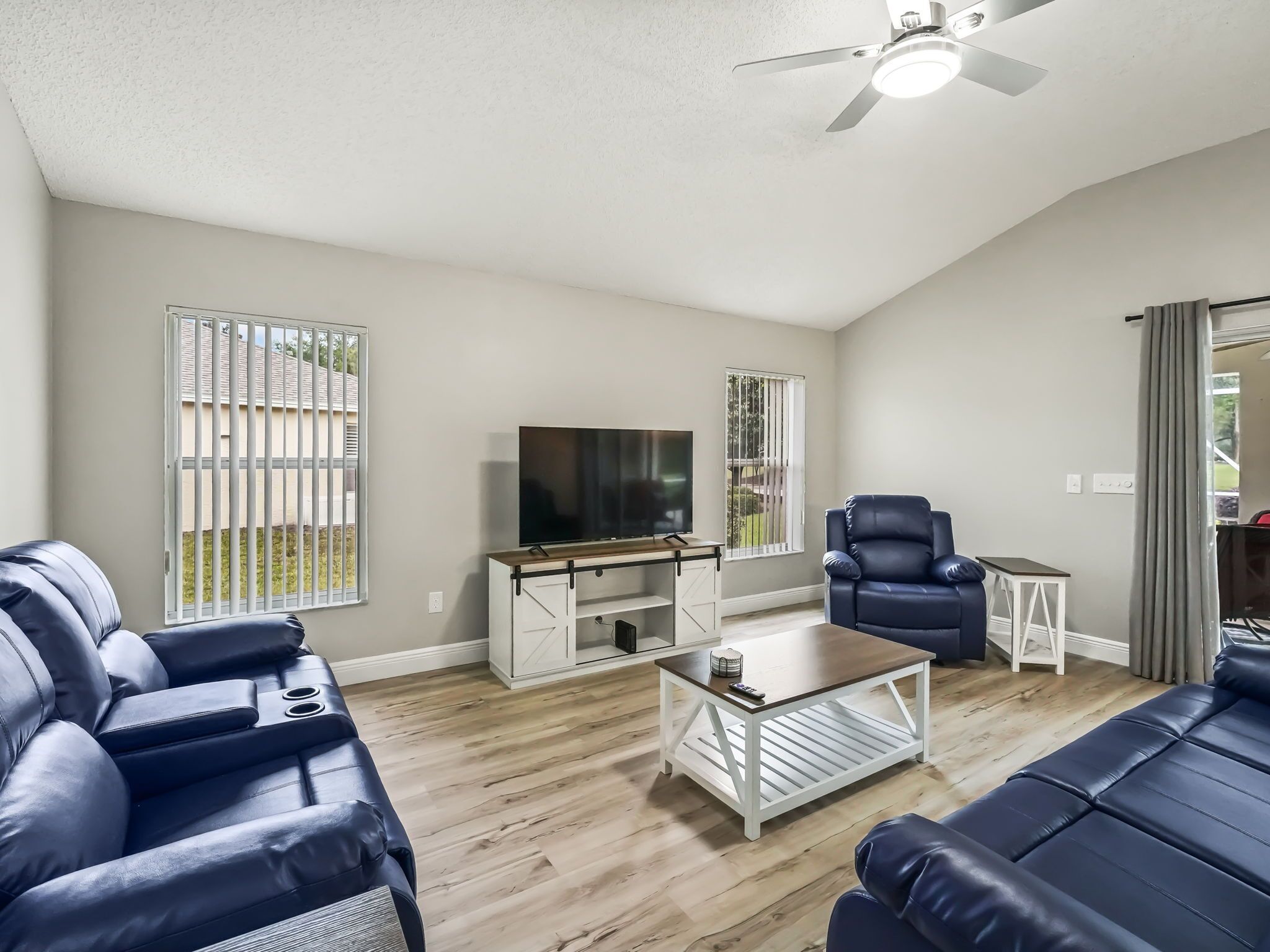 A spacious living room with a flat-screen TV, leather sofas, a coffee table, and a ceiling fan.