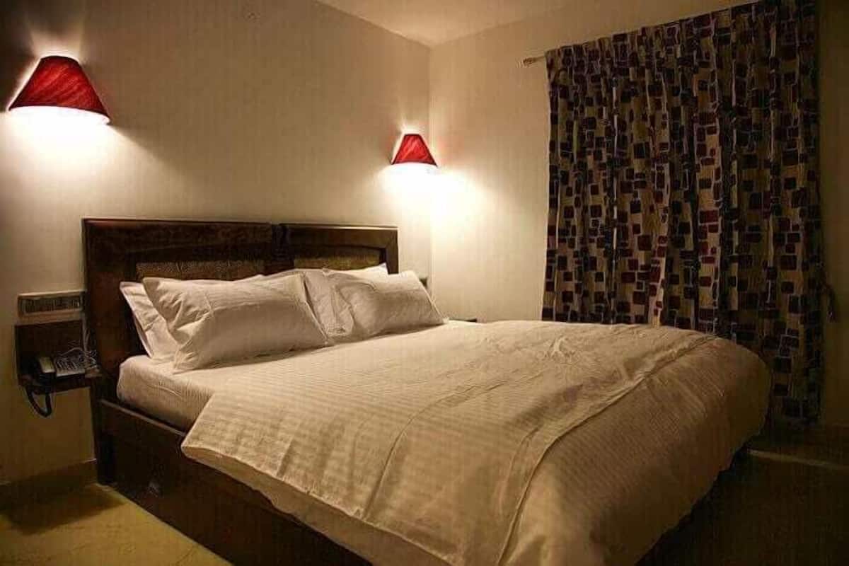 A hotel room with a large bed, two bedside lamps, a telephone, and a patterned curtain.