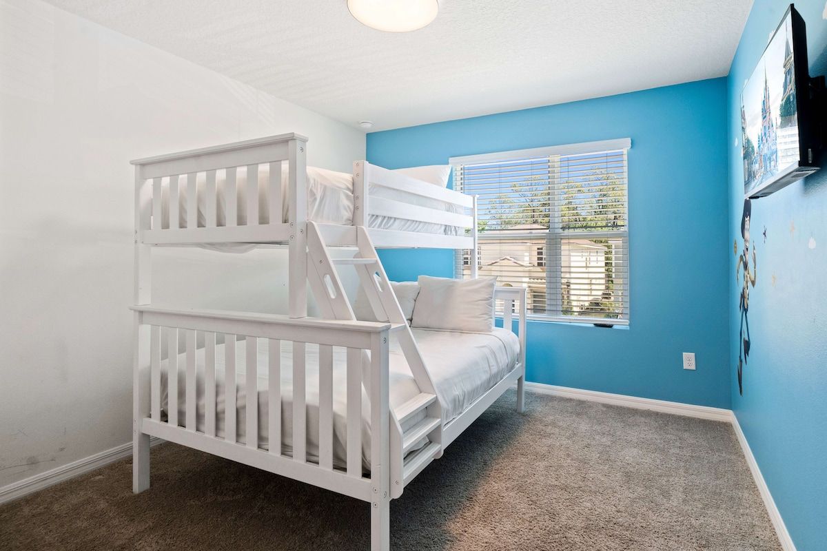 Une chambre avec un lit superposé, une fenêtre avec des stores et un téléviseur fixé au mur.