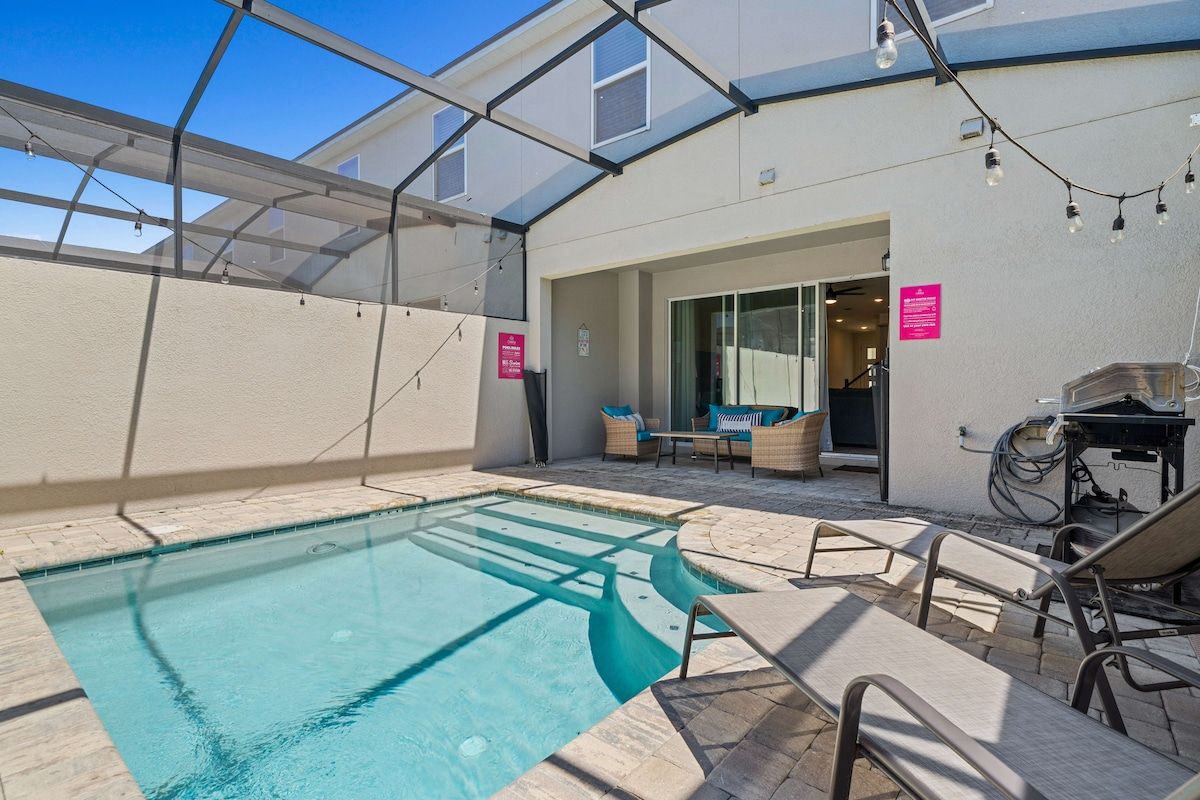 A swimming pool with a glass enclosure, outdoor seating, and a covered patio area.
