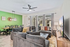 A modern living room with grey sofas, a dining table, and a ceiling fan. - Disney Themes: Resort 5BR Townhouse w Private Pool (Kissimmee)