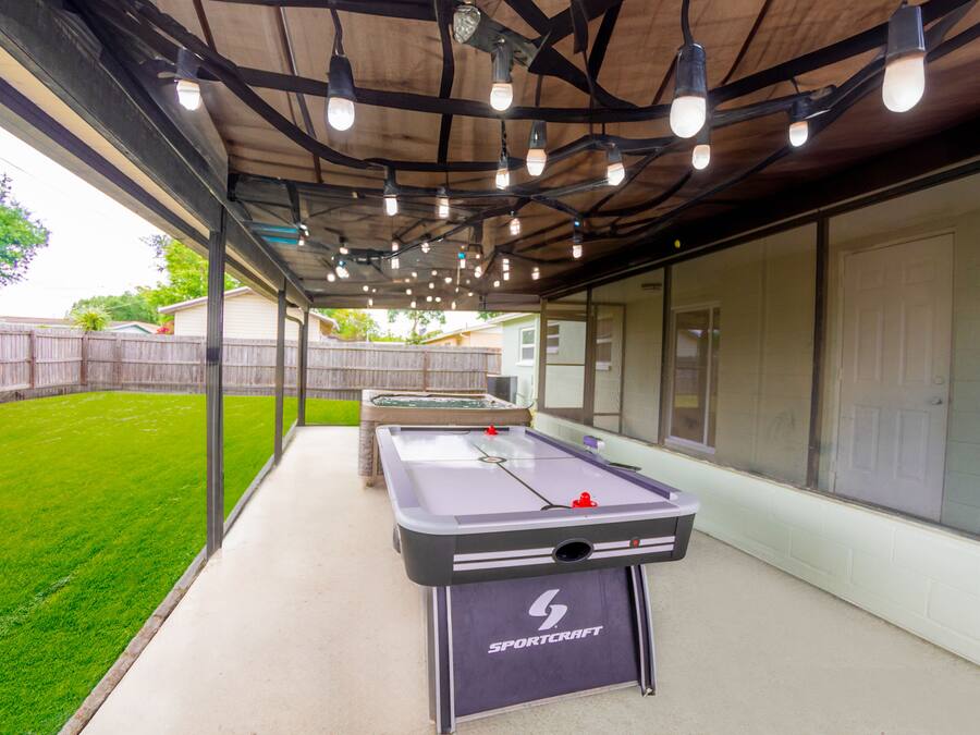 Zona de billar exterior con una mesa Sportcraft, rodeada por un porche cubierto con luces colgantes.