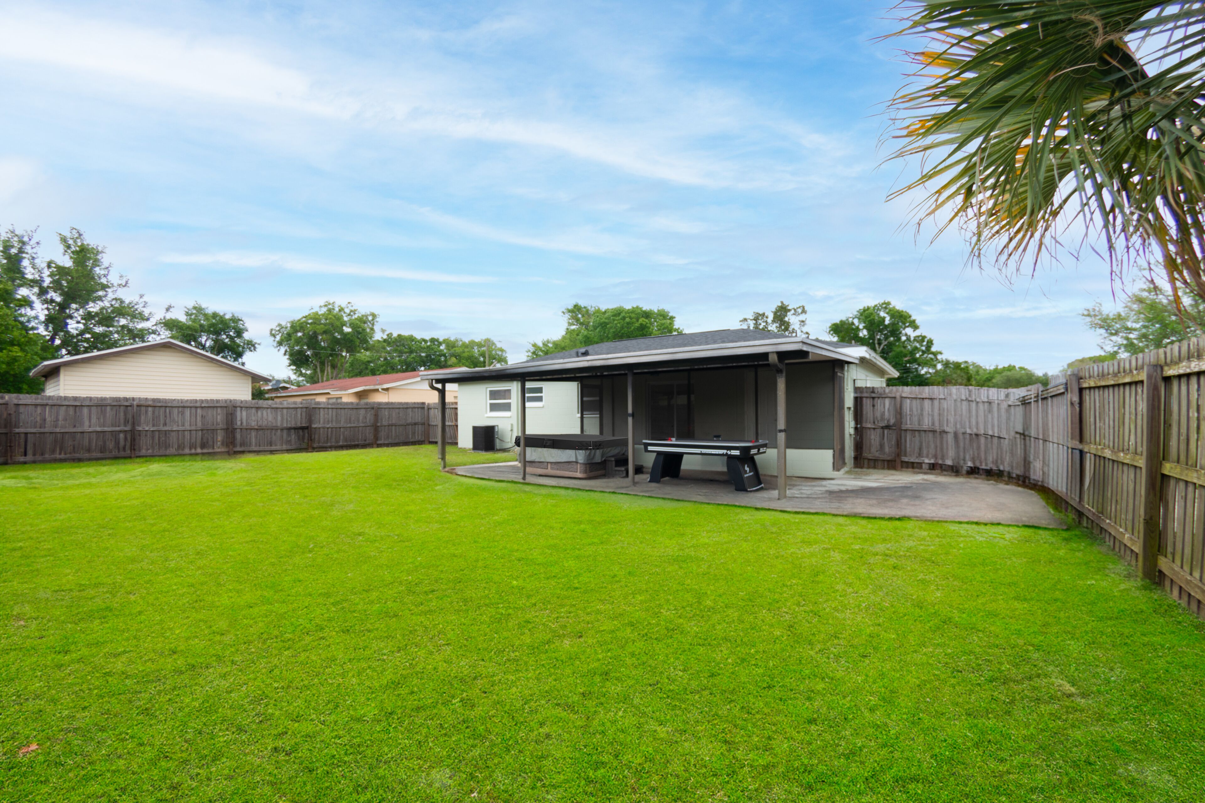 A backyard with a covered patio, a pool table, and a wooden fence.