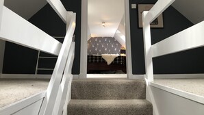 Una escalera conduce a un dormitorio con una pared oscura y un cabecero estampado.