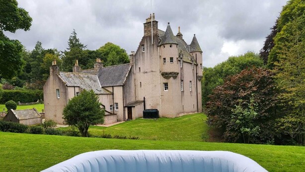 Un edificio grande, de estilo castillo, con un césped bien cuidado y una piscina inflable pequeña al frente.