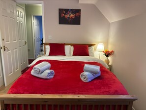 Ein Hotelzimmer mit einem großen Bett, roter und weißer Bettwäsche, zwei zusammengerollten Handtüchern auf dem Bett, einem Nachttisch mit einer Lampe und einem Bild an der Wand.