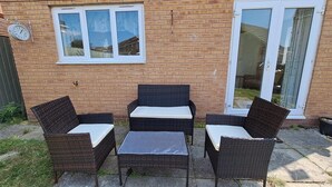 En terrasse med fletmøbler, en murstensvæg og et vindue med et ur.