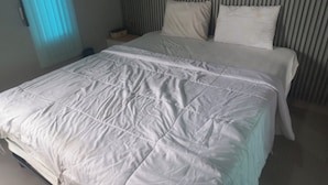 A neatly made bed with a white duvet and pillows, a bedside table with a lamp, and a window with blinds. - Capital O 93816 Cerry Village (Tegal)