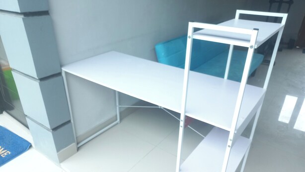 A white metal desk with a blue storage bin in a room with tiled flooring. - Capital O 93816 Cerry Village (Tegal)