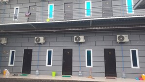 A building with multiple black doors and windows, air conditioning units, and a concrete ground. - Capital O 93816 Cerry Village (Tegal)