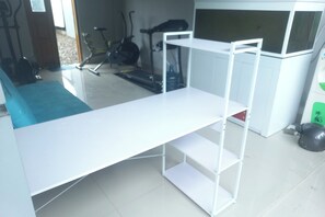 A white desk with a shelf, a treadmill, and a bicycle in the background.