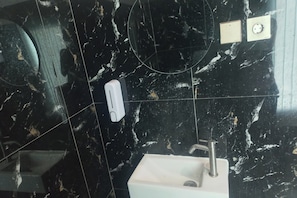 A bathroom with a sink, a mirror, and a soap dispenser on the wall.