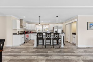 A modern kitchen with white cabinets, a central island with bar stools, and a herringbone wood floor. - 705 Shortoff Cottage: Modern 3BR Cottage w/ Firepit & EV Charger | Pet Friendly (Highlands)