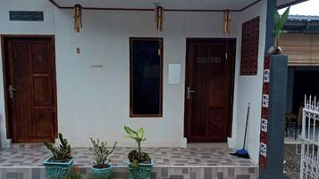 Un edificio con tres puertas de madera, un vestíbulo con azulejos y plantas en macetas.