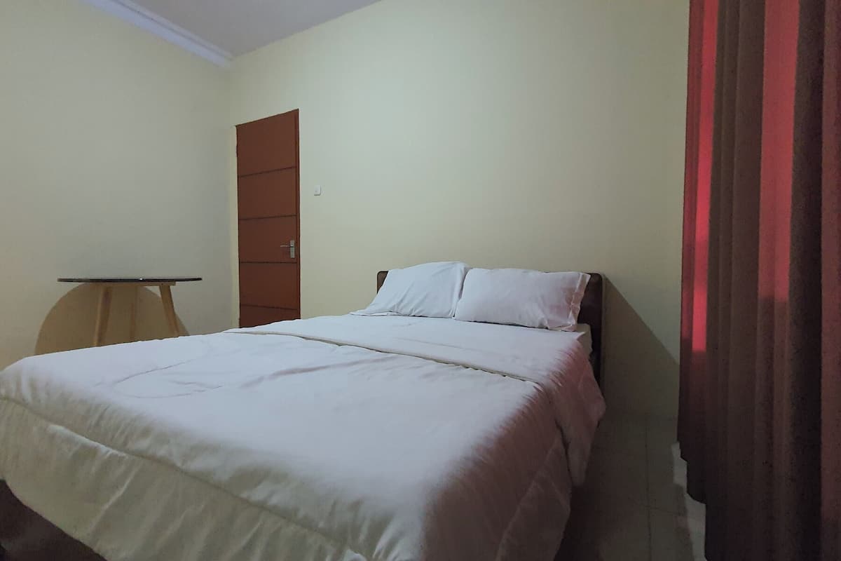 Habitación individual con una puerta de madera, una mesita pequeña y una cortina a la derecha.