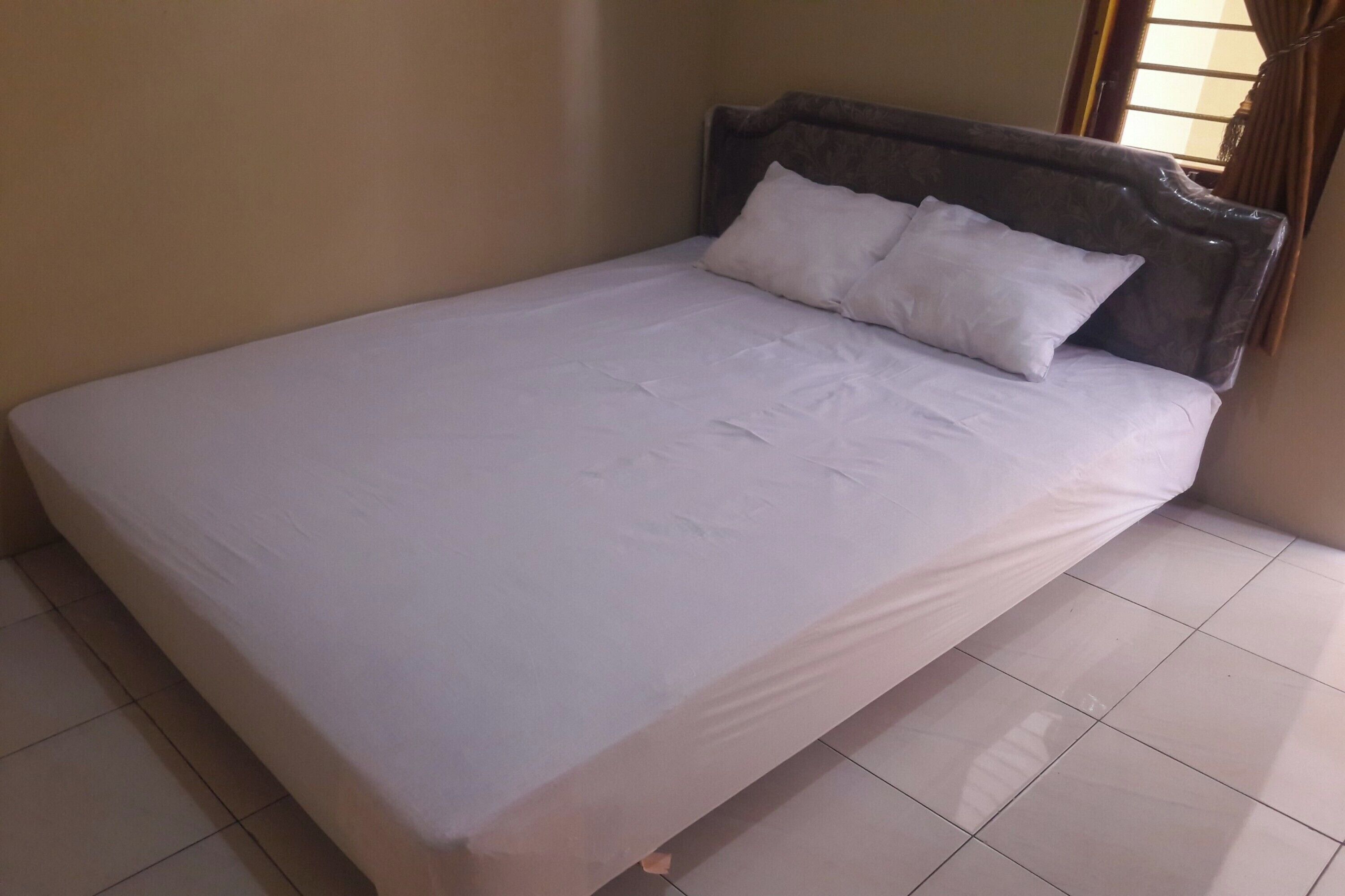 A neatly made bed with white linens and a wooden headboard in a room with tiled flooring.