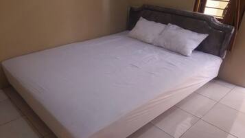 A neatly made bed with white linens and a wooden headboard in a room with tiled flooring.