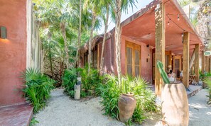 A rustic building with a thatched roof, surrounded by lush greenery and palm trees. - Jungle Studios on Beach Road with Pool  (Tulum)