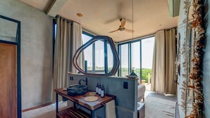 A bathroom with a large window, a wooden vanity, a ceiling fan, and a view of the outdoors.